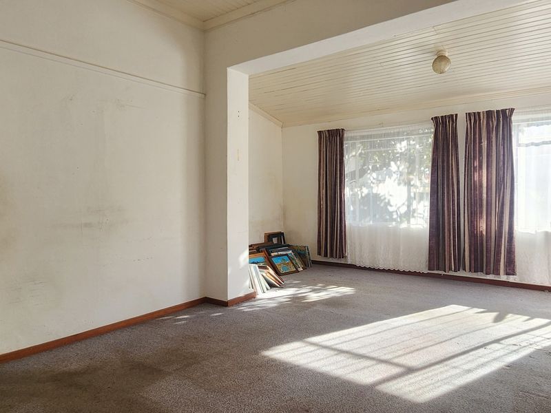 An empty living room featuring an arched entryway, timber-paneled ceilings, and large windows, requiring cosmetic updates to the walls and flooring.