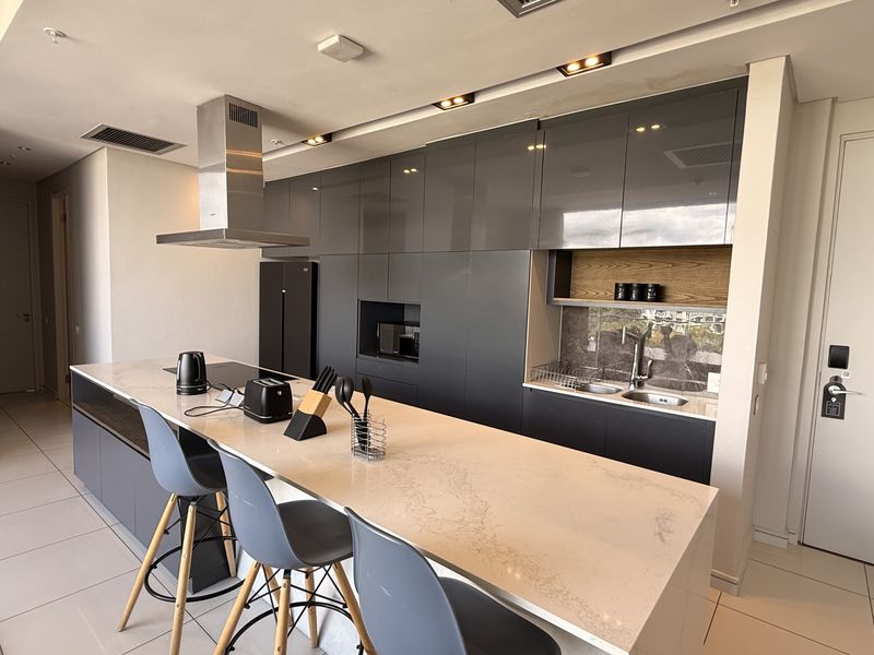 Modern kitchen featuring high-gloss grey cabinetry, a large stone-topped island, integrated appliances, and sleek recessed lighting in an open-plan penthouse layout.