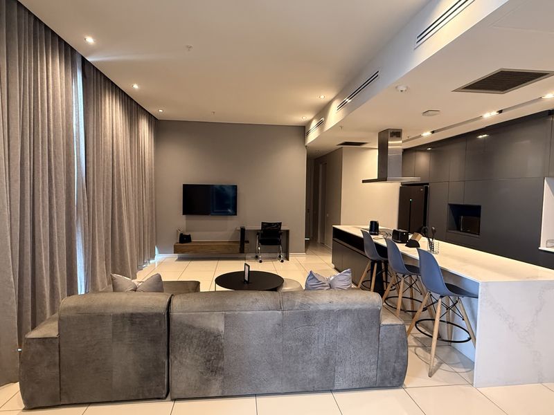 Modern open-plan living area featuring a sleek kitchen with stone island, integrated cabinetry, ducted air conditioning, and floor-to-ceiling curtains.