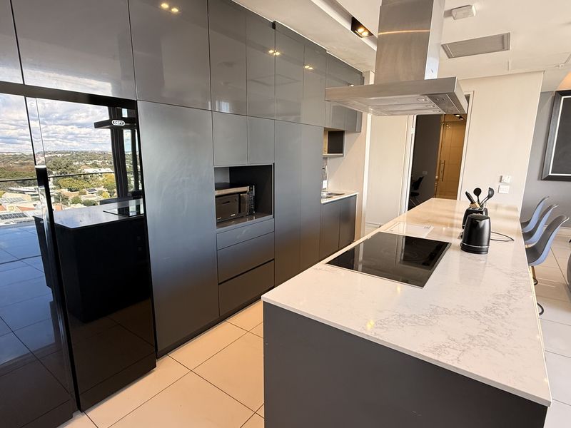 Modern open-plan kitchen featuring high-gloss grey cabinetry, a stone-topped island with an integrated induction hob, and sleek contemporary finishes.