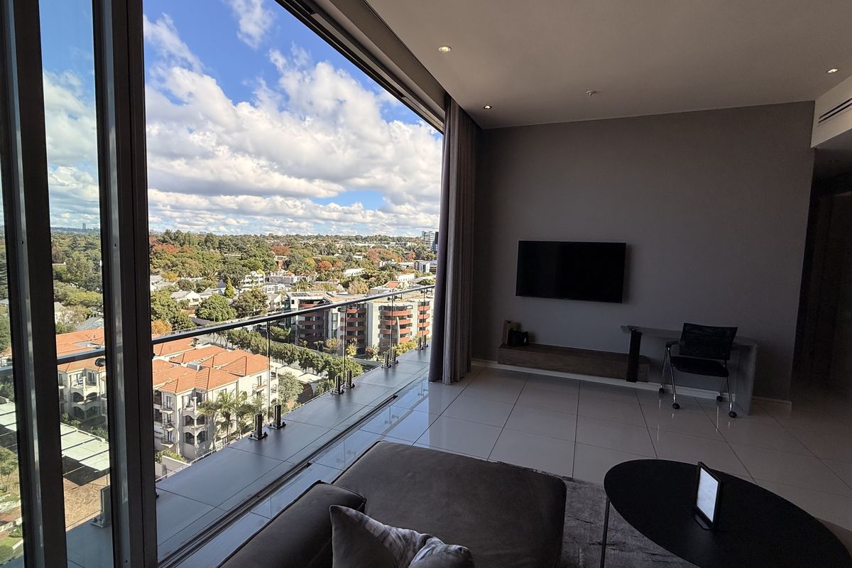Modern penthouse living area featuring expansive floor-to-ceiling sliding doors that open to a balcony with panoramic urban views and high-quality tiled flooring.