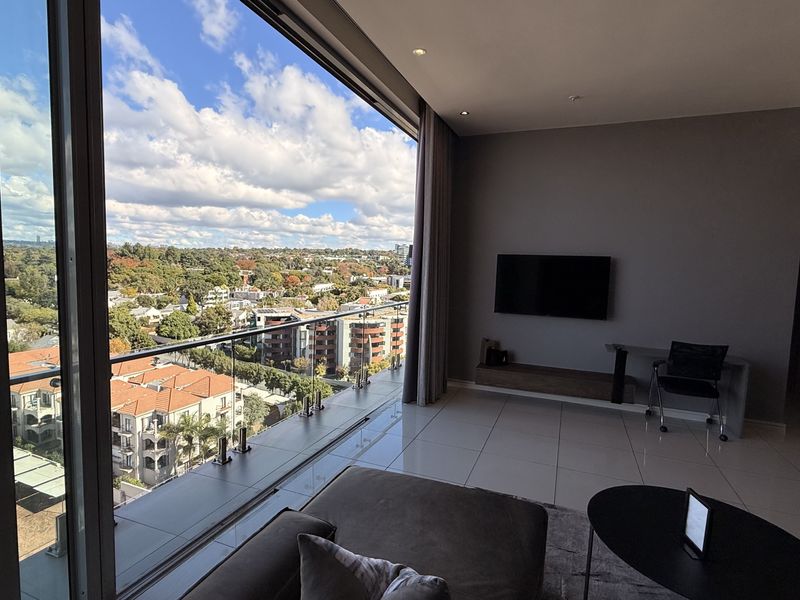 Modern penthouse living area featuring expansive floor-to-ceiling sliding doors that open to a balcony with panoramic urban views and high-quality tiled flooring.