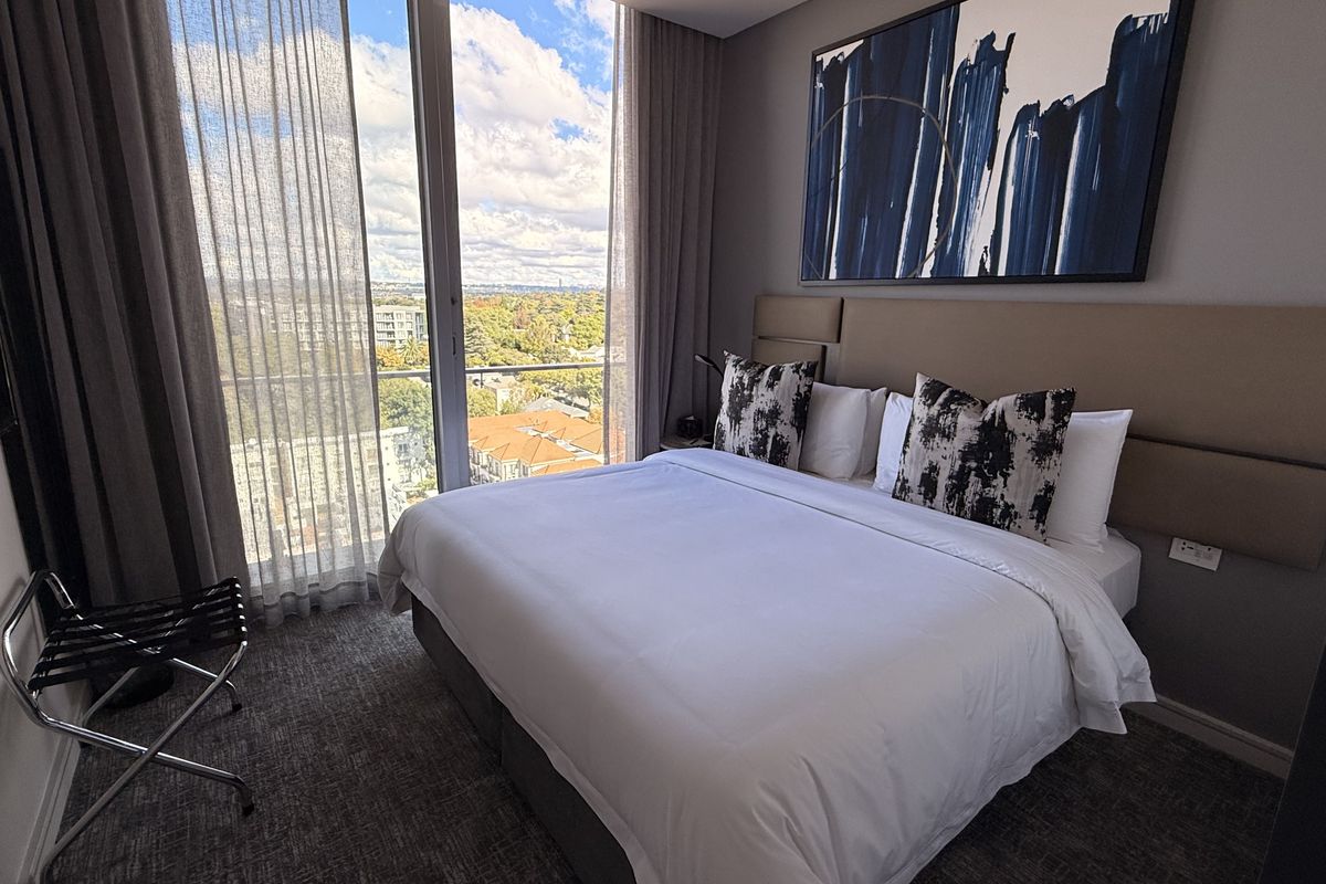 A modern penthouse bedroom featuring floor-to-ceiling windows with expansive city views, a custom upholstered headboard, and high-quality finishes.