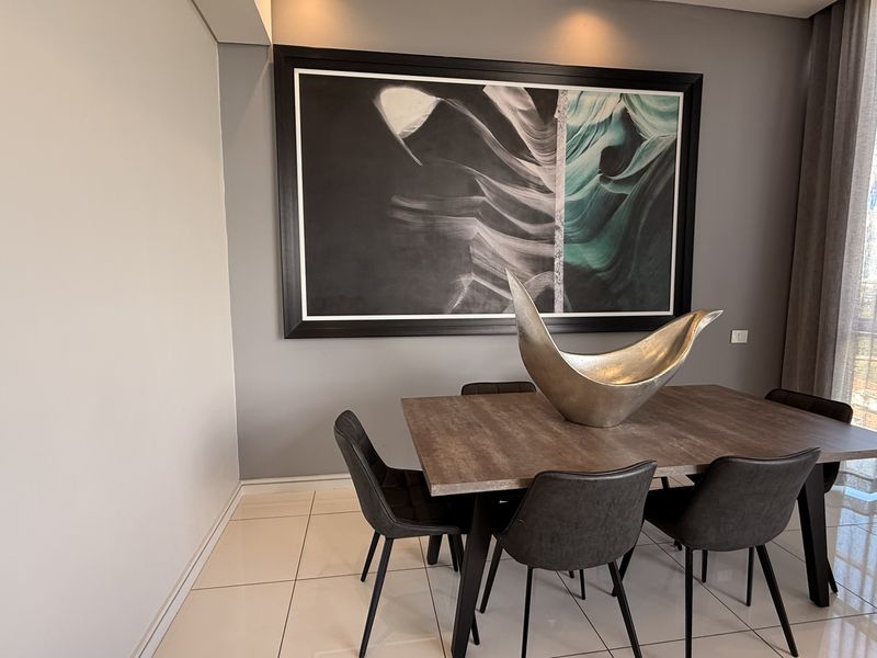 A modern dining room featuring polished tiled flooring, recessed lighting, and large floor-to-ceiling windows offering natural light and expansive views.