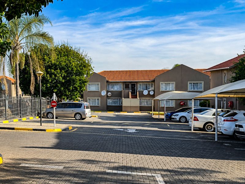Exterior view of an apartment complex featuring a paved parking area, covered carports, and well-maintained building facades with tiled roofing.