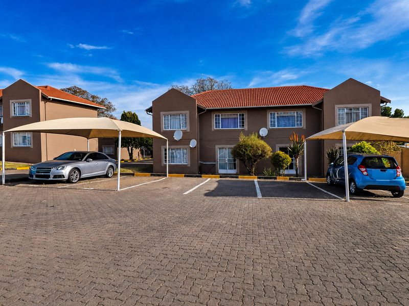 Front view of a multi-story apartment complex featuring paved parking areas with shade cloth carports and well-maintained exterior facades.