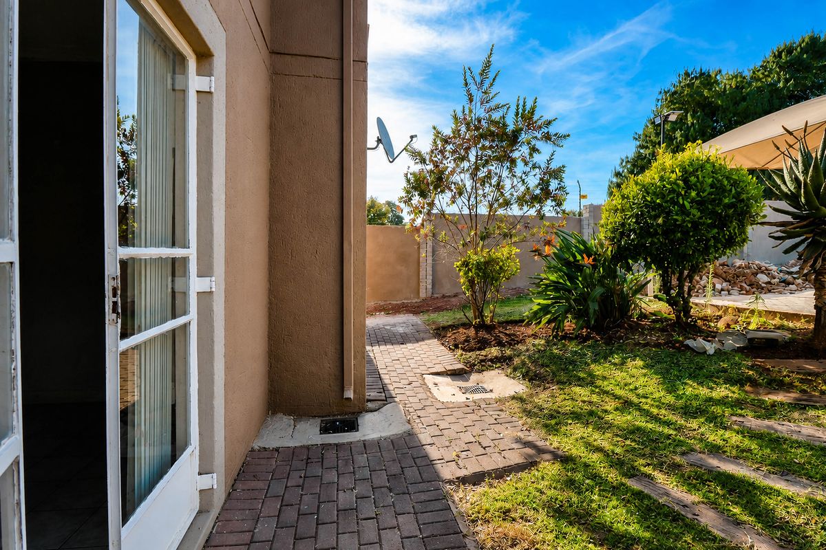 A view of the rear exterior area featuring a paved walkway, landscaped garden, and access to the interior through a glass door.