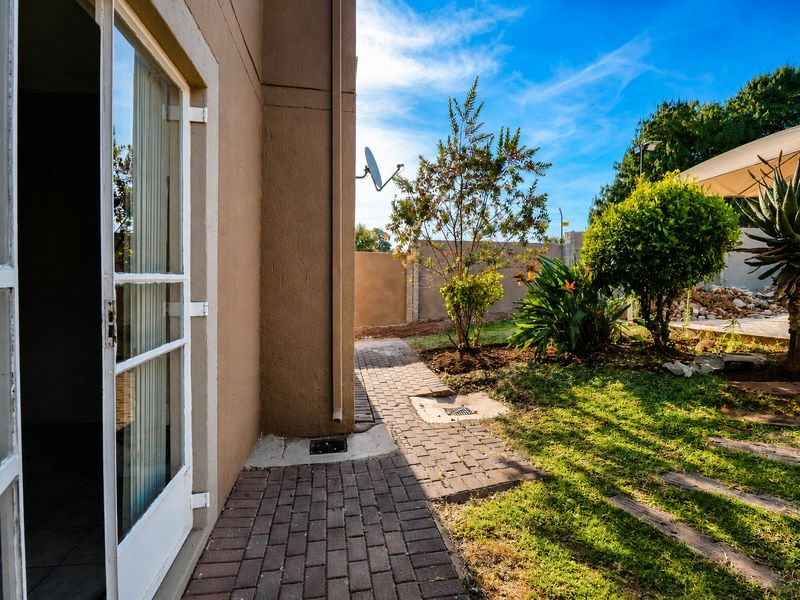 A view of the rear exterior area featuring a paved walkway, landscaped garden, and access to the interior through a glass door.