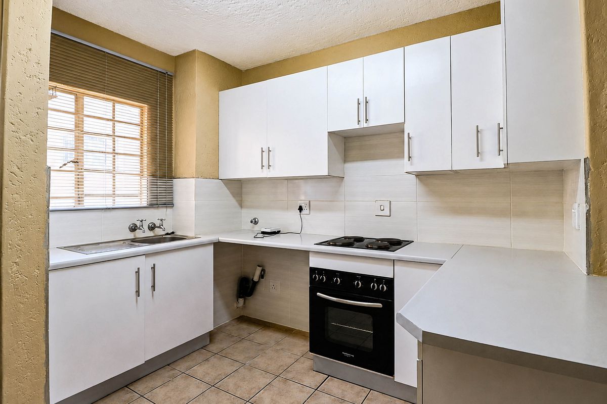 A functional kitchen featuring white cabinetry, laminate countertops, a built-in oven and hob, and tiled flooring, offering a clean and practical workspace.