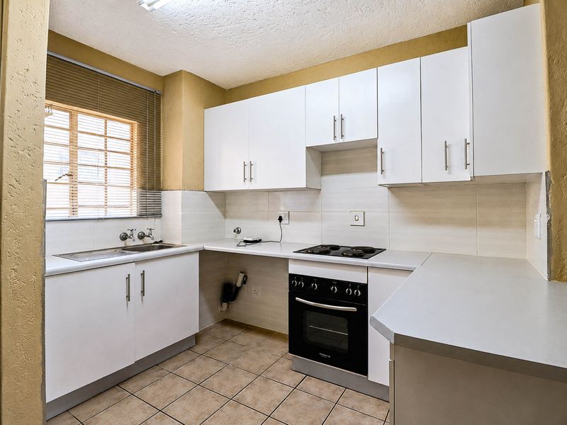 A functional kitchen featuring white cabinetry, laminate countertops, a built-in oven and hob, and tiled flooring, offering a clean and practical workspace.