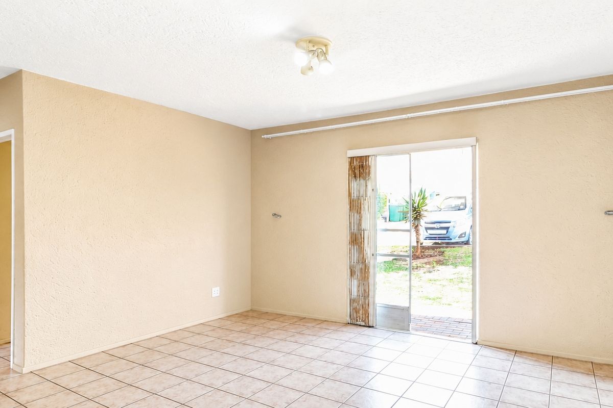 A bright, empty living room featuring neutral tiled flooring and a sliding glass door providing direct access to the exterior.