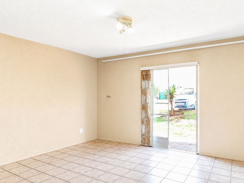 A bright, empty living room featuring neutral tiled flooring and a sliding glass door providing direct access to the exterior.