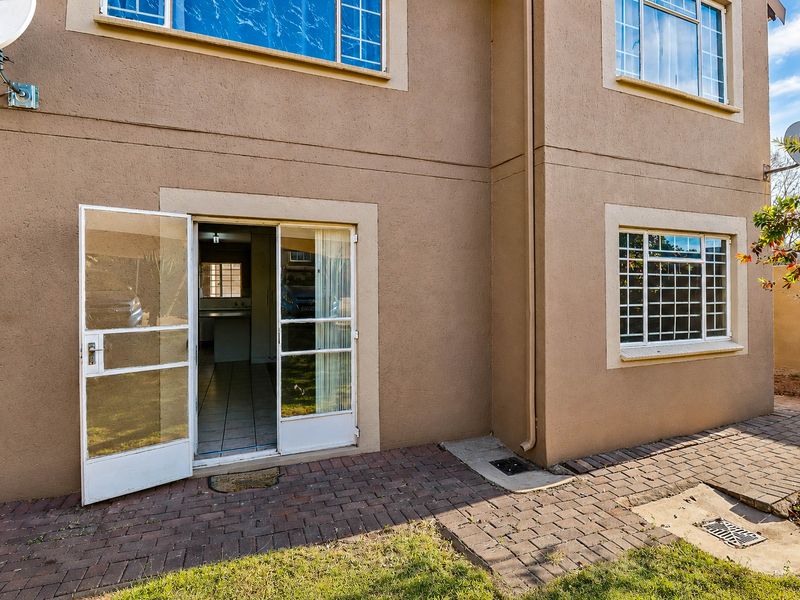 Rear exterior view of the apartment featuring a paved patio area, sliding glass door with security gate, and standard aluminium window frames.