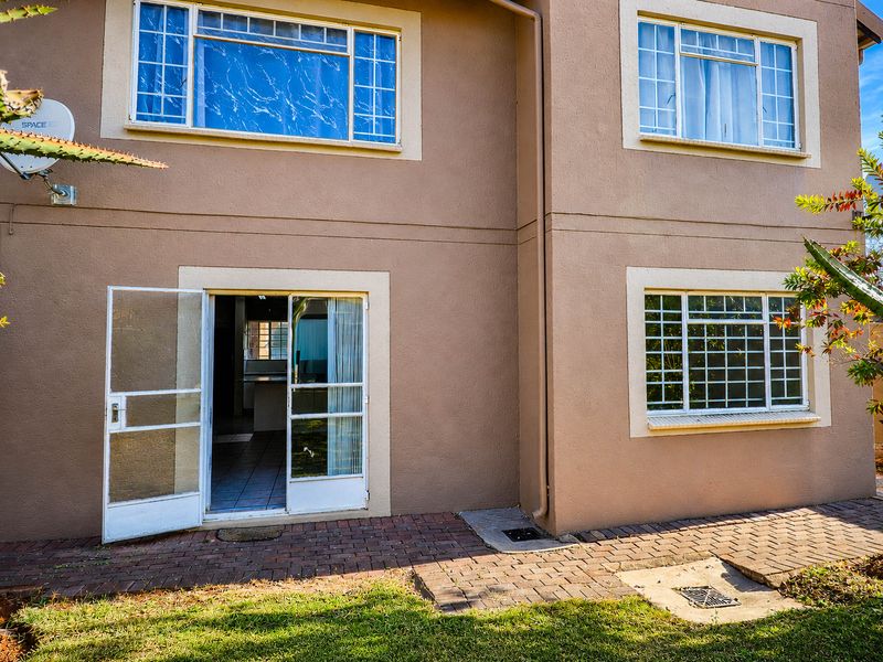 Rear exterior view of the apartment featuring a paved patio area, security gates, and window burglar bars.