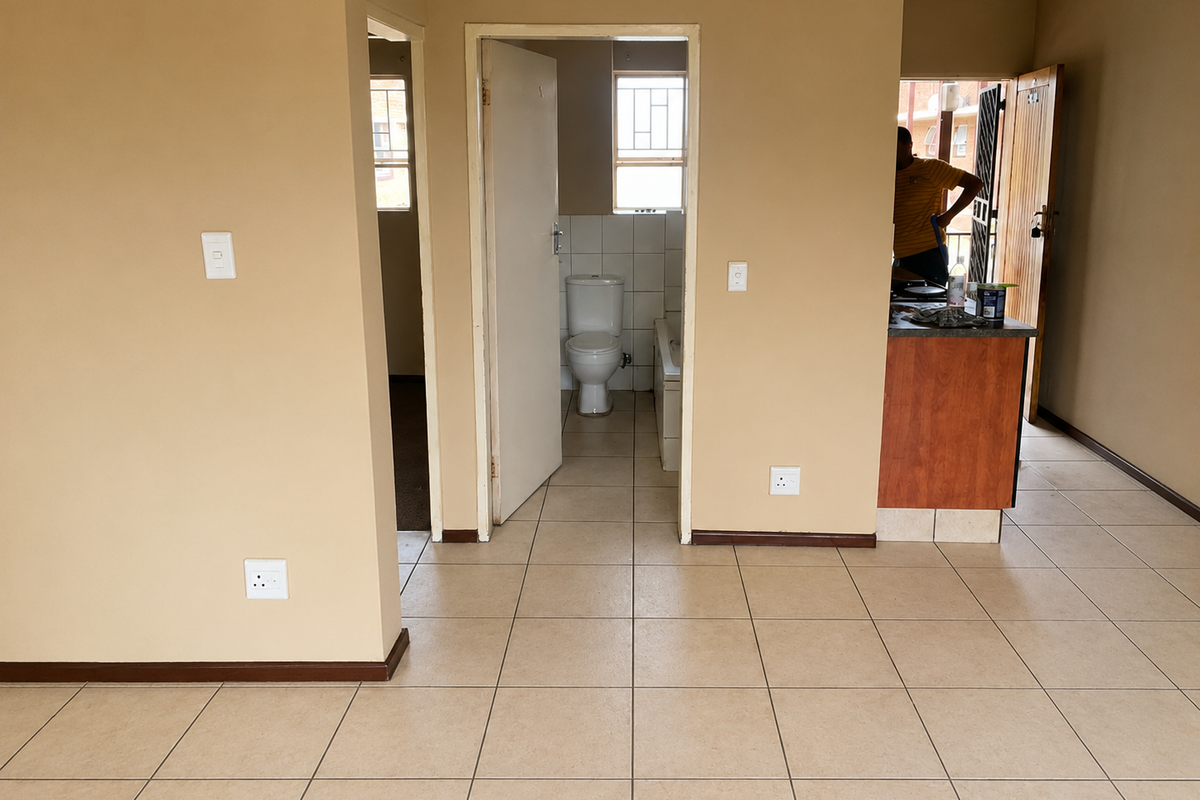 Open plan living area featuring tiled flooring, neutral wall tones, and direct access to a bathroom and kitchen area with built-in cabinetry.