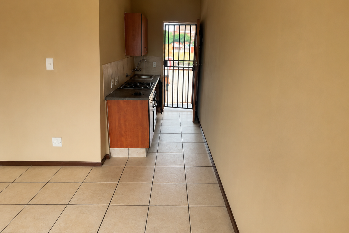 Compact kitchen area featuring built-in cabinetry, gas hob, and tiled flooring, leading directly to an exterior security gate.