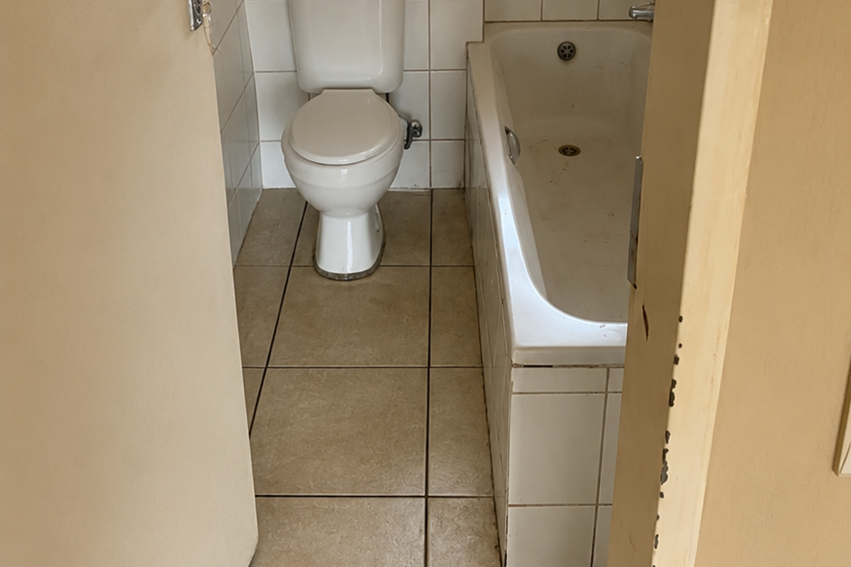 A compact bathroom featuring a standard bathtub, toilet, tiled flooring, and tiled wall surrounds with security bars on the window.