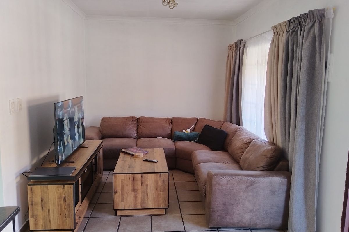 A functional living room featuring ceramic floor tiles, neutral wall finishes, and large window treatments, providing a comfortable and well-lit space.
