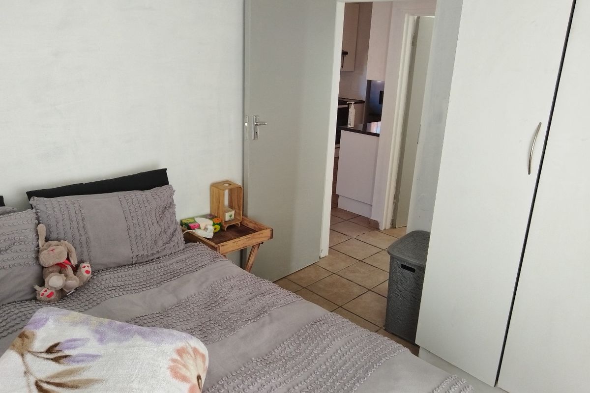 A bedroom featuring tiled flooring and a built-in wardrobe, with a view through the doorway into the adjacent kitchen area.