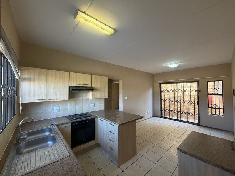 Open-plan kitchen and living area featuring tiled flooring, built-in cabinetry with laminate countertops, and direct access to an outdoor space via a security gate.