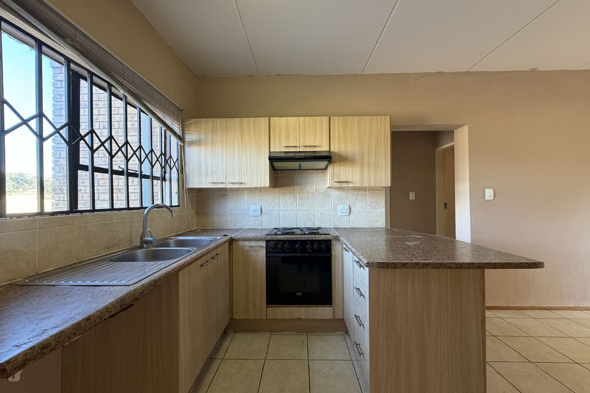 A functional kitchen featuring light wood-finish cabinetry, granite-look laminate countertops, a built-in oven with hob, and tiled flooring.