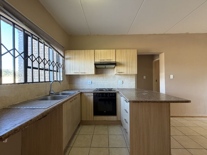 A functional kitchen featuring light wood-finish cabinetry, granite-look laminate countertops, a built-in oven with hob, and tiled flooring.