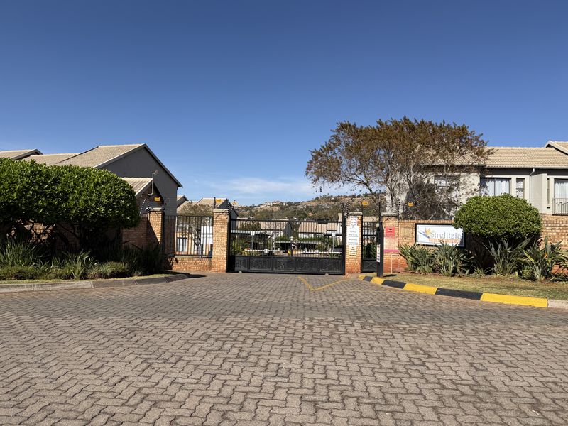 The entrance to Strelitzia complex featuring secure gated access, brick paving, and established landscaping.