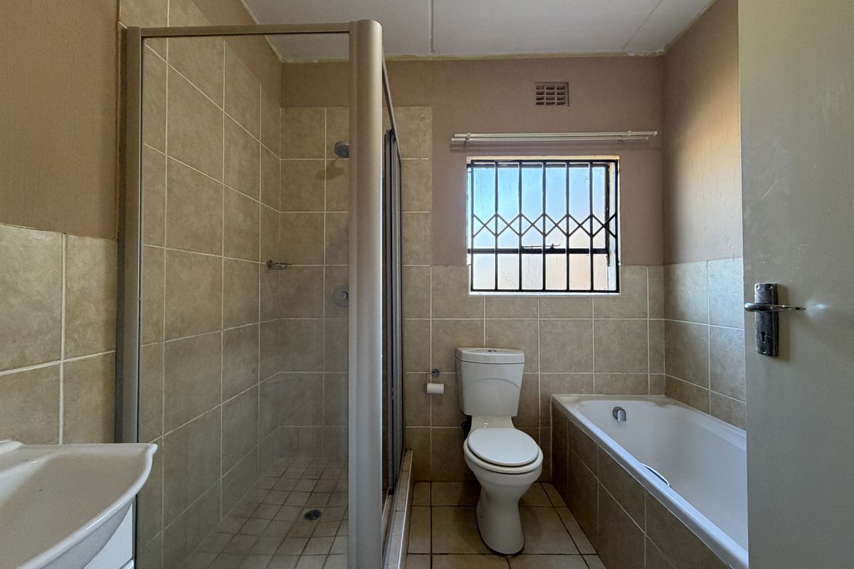 A functional bathroom featuring a separate shower enclosure, bathtub, and toilet, with neutral wall and floor tiling throughout.