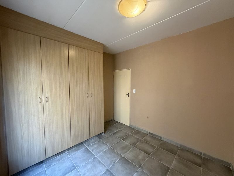 An empty bedroom featuring tiled flooring and built-in wooden cupboards, providing a neutral canvas for personalization.