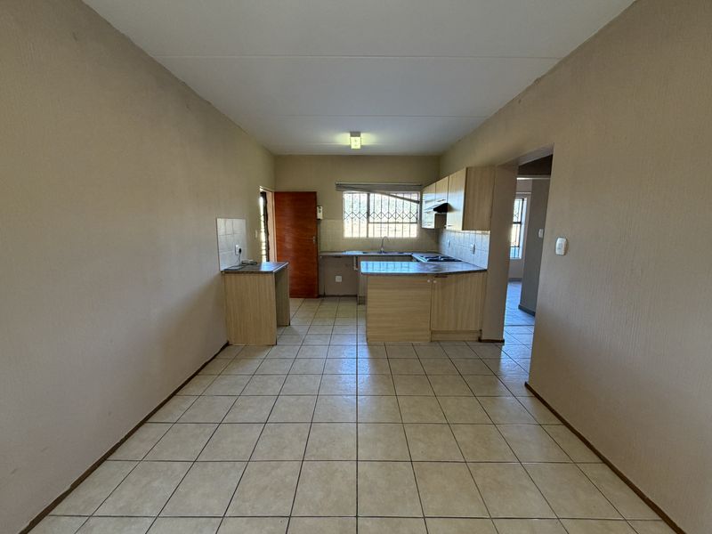 An empty kitchen featuring laminate cabinetry, built-in hob, extractor fan, and ceramic floor tiles, offering a functional layout ready for modernization.