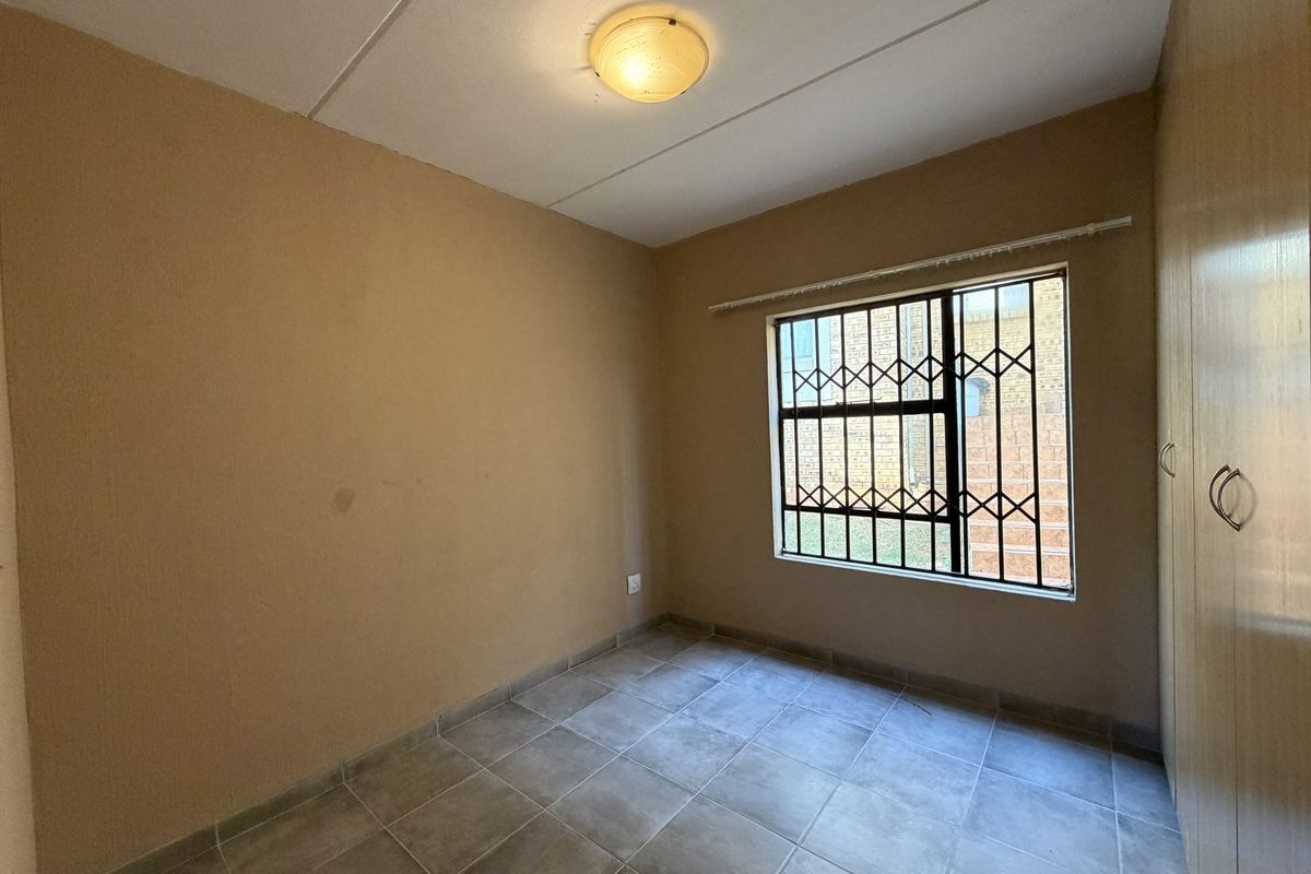 An empty bedroom featuring tiled flooring, built-in cupboards, and a window fitted with security bars.