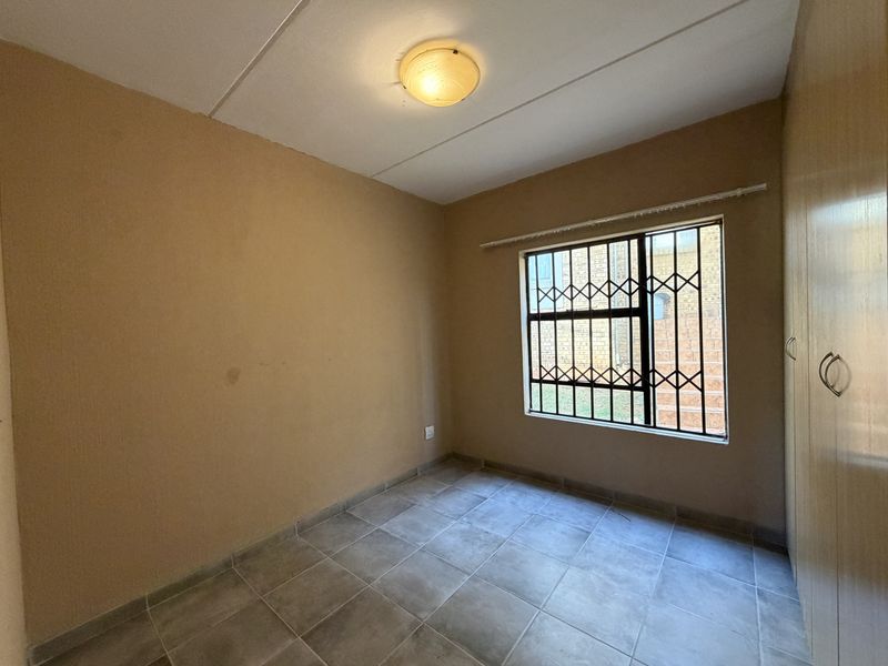 An empty bedroom featuring tiled flooring, built-in cupboards, and a window fitted with security bars.