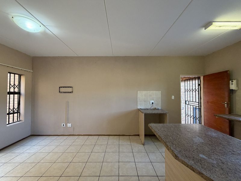 An empty open-plan living and kitchen area featuring tiled flooring, a built-in breakfast counter, and direct access to an exterior security gate.