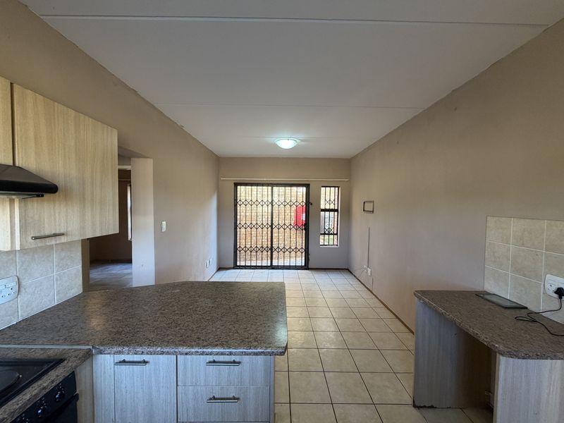 Open-plan kitchen and living area featuring tiled flooring, laminate cabinetry, built-in oven, and a secure sliding door leading to the exterior.