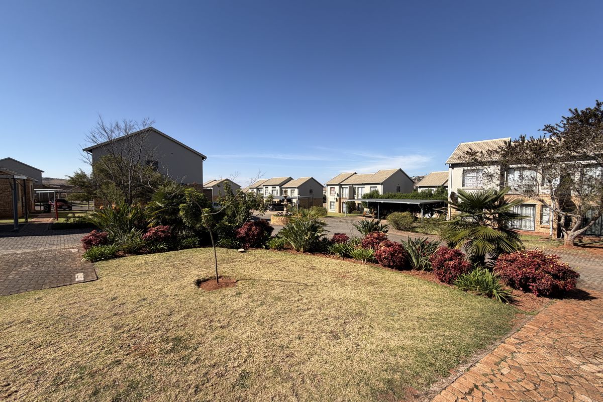 A view of the apartment complex grounds featuring a well-maintained lawn, landscaped garden beds, paved walkways, and covered carport parking areas.