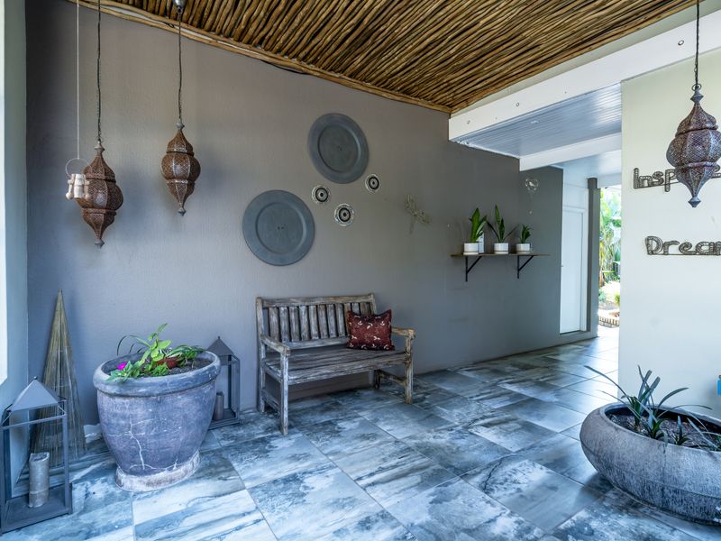 A covered patio area featuring a rustic thatched ceiling, tiled flooring, and neutral wall finishes, providing a comfortable outdoor living space.