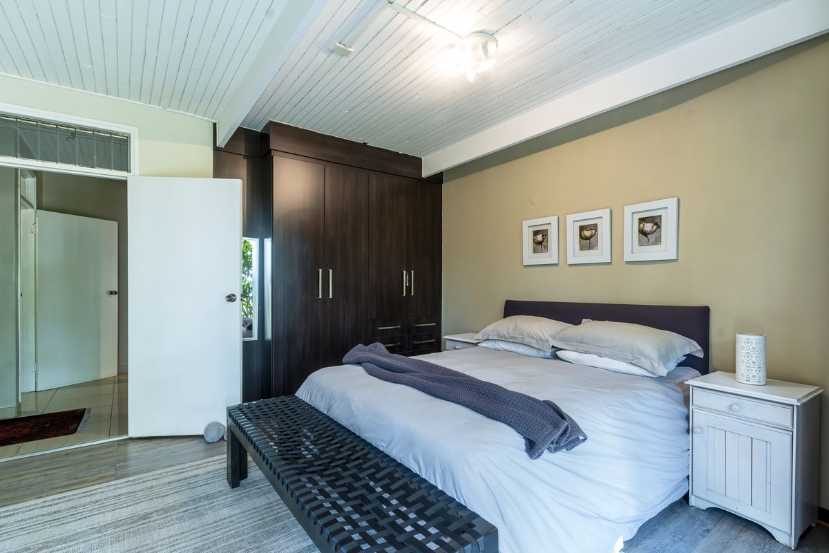 A well-maintained bedroom featuring dark wood built-in cupboards, light timber-look flooring, and a classic tongue and groove ceiling.