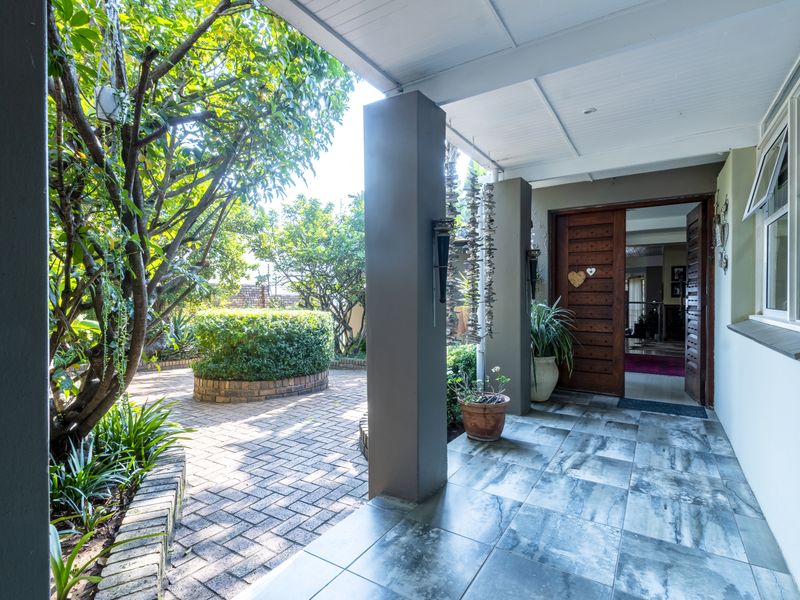 A covered patio entrance featuring tiled flooring, leading to a private brick-paved courtyard with established garden landscaping.