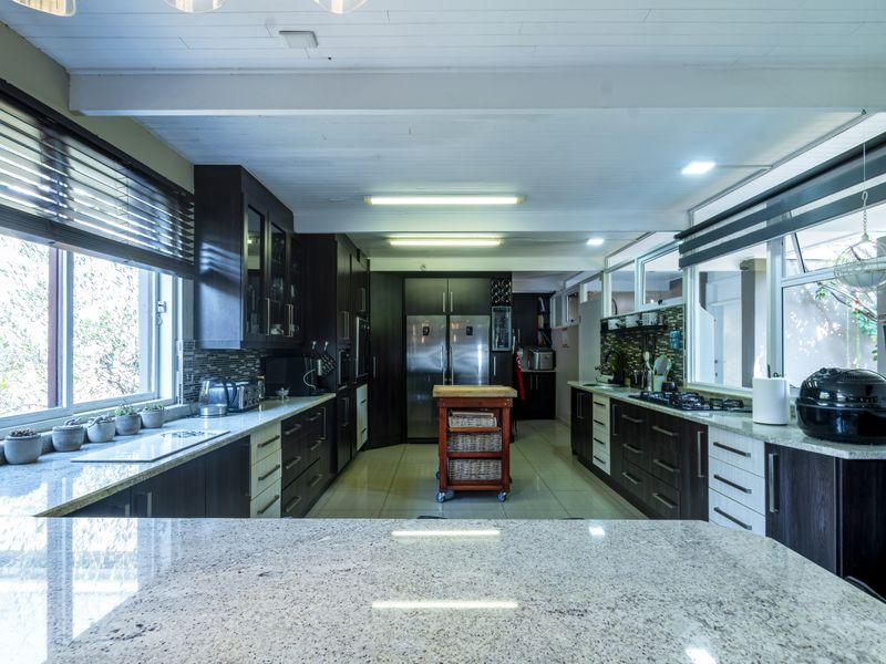 Spacious modern kitchen featuring dark wood cabinetry, granite countertops, integrated appliances, and ample natural light from large windows.