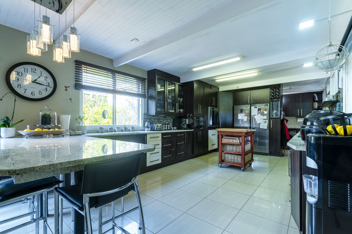 Modern kitchen featuring dark wood cabinetry, granite countertops, tiled flooring, and an exposed beam ceiling with contemporary pendant lighting.