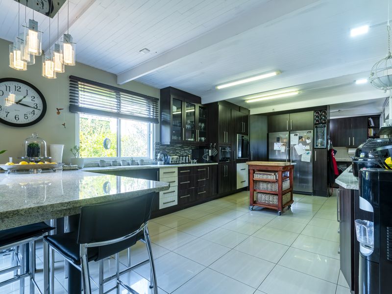 Modern kitchen featuring dark wood cabinetry, granite countertops, tiled flooring, and an exposed beam ceiling with contemporary pendant lighting.