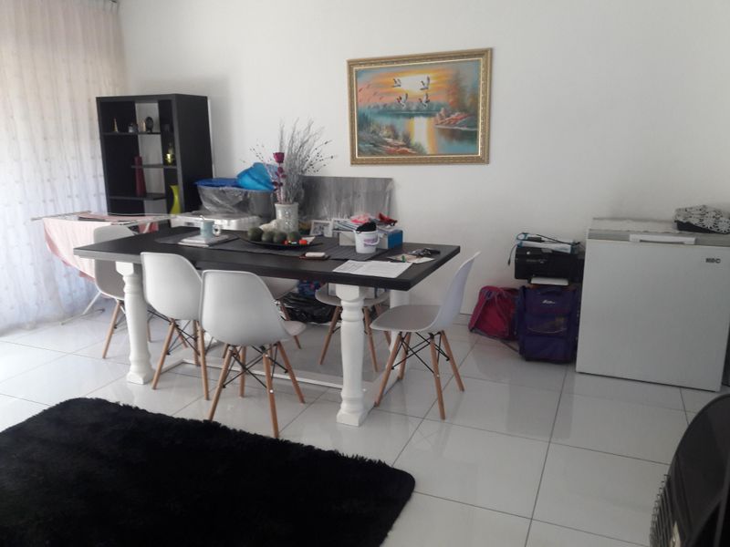 A dining area featuring neutral tiled flooring and large windows with curtain tracks, providing a bright and functional space for meals.