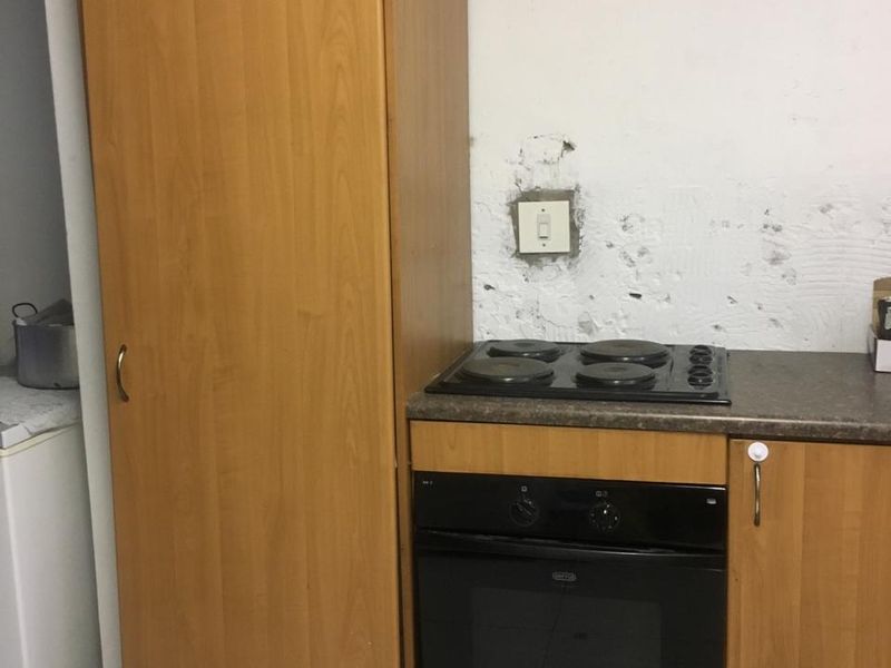 A small kitchen area featuring built-in cabinetry, an oven, and an electric hob, requiring wall repairs and cosmetic updates.