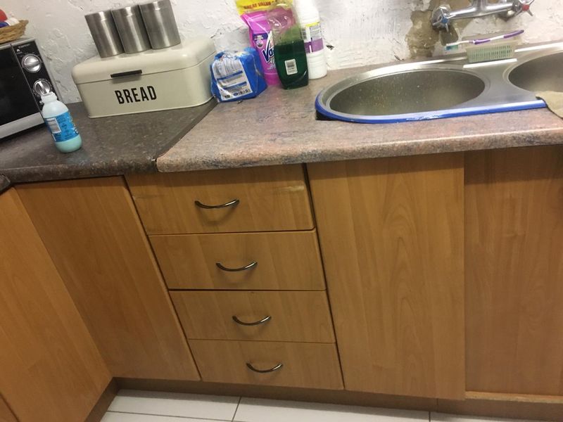 A dated kitchen area featuring wooden cabinetry, laminate countertops, and a double bowl sink, currently showing signs of wear and wall damage.