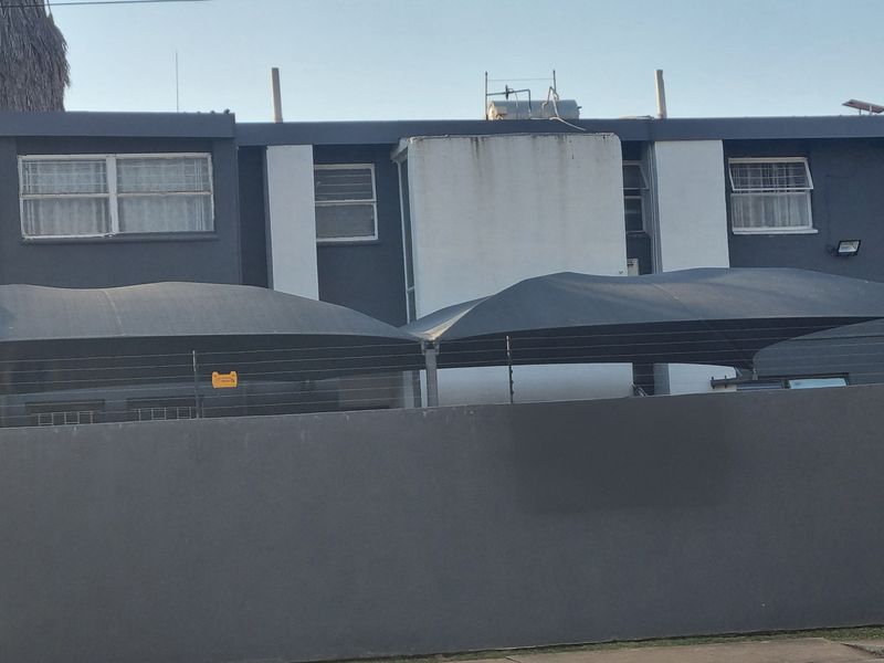 Front elevation of a townhouse complex featuring a solid boundary wall, electric fencing, and multiple shade sail carports over the parking area.