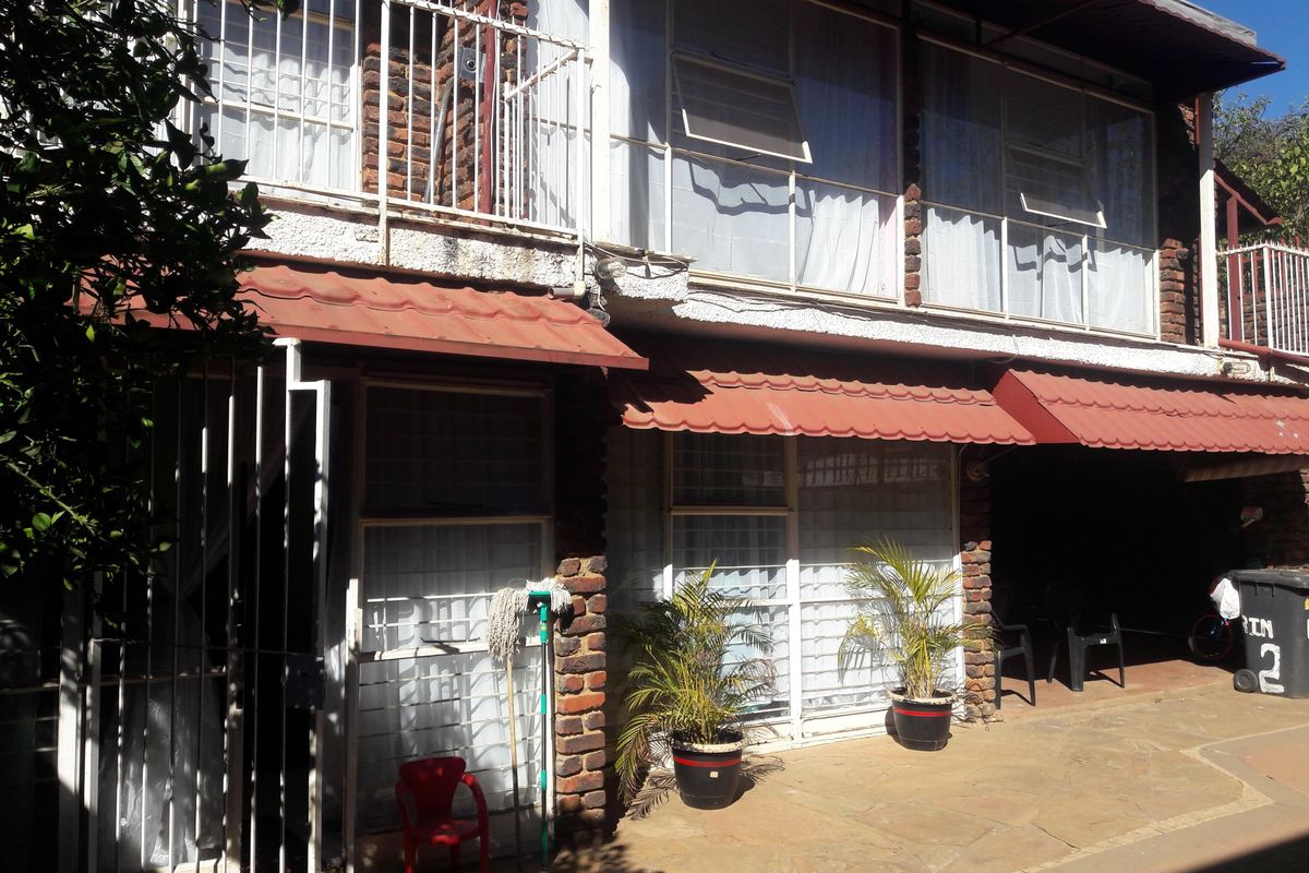 Rear exterior view of a two-story townhouse featuring exposed brickwork, a ground-level tiled patio, and an upper-level balcony with metal security railings.