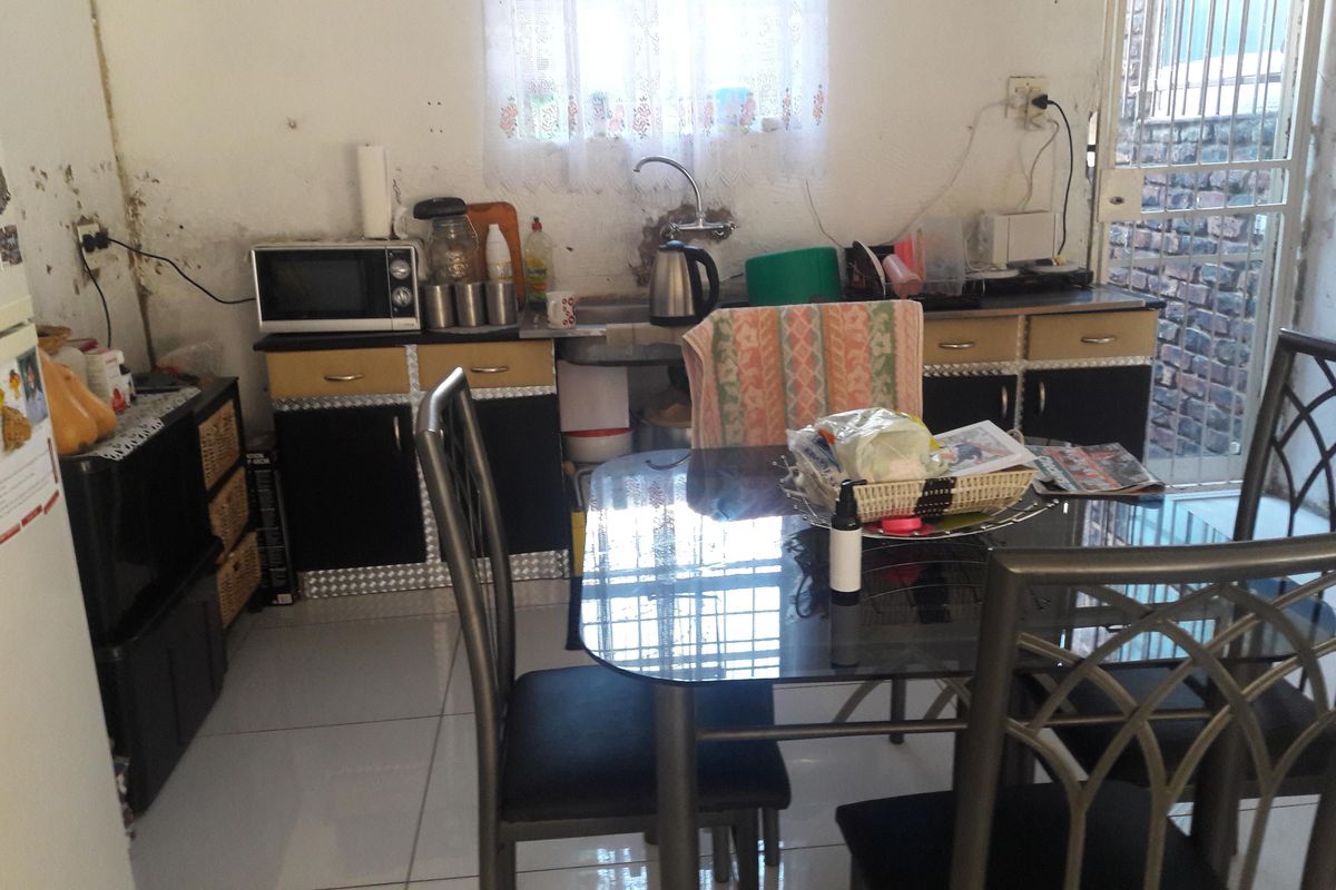 A compact kitchen area featuring tiled floors, basic cabinetry, and a sink, currently showing significant wall surface wear and deterioration.