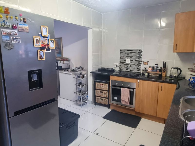 Functional kitchen featuring wooden cabinetry, built-in oven and hob, tiled splashbacks, and tiled flooring with an adjacent scullery area.