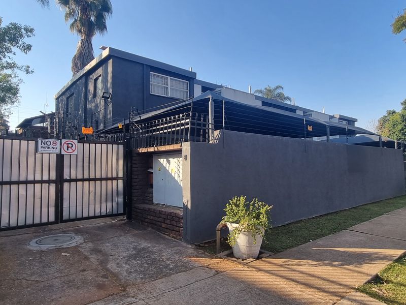 Front exterior view of the townhouse property featuring a secure gated entrance, perimeter wall with electric fencing, and a paved driveway.