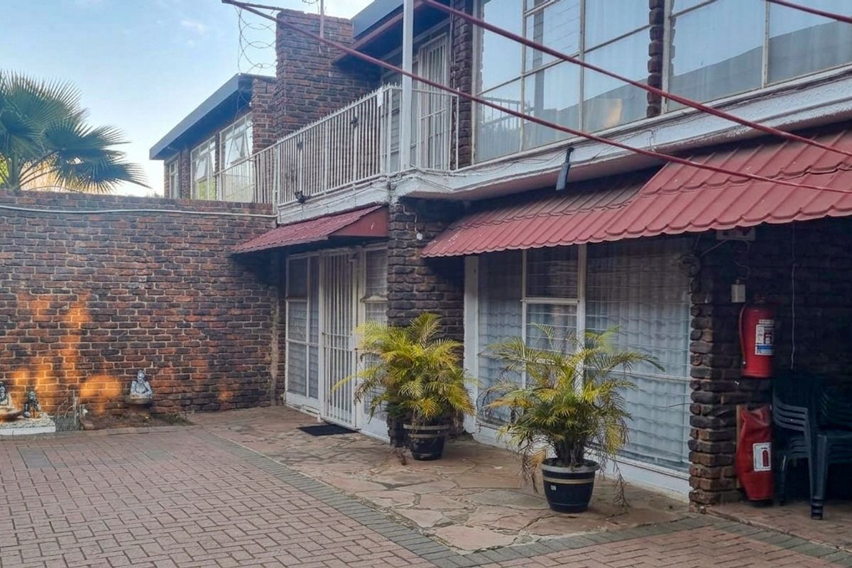 Rear exterior view of a townhouse featuring a paved courtyard, brick facade, balcony with metal railings, and protective awnings over the ground floor entrances.